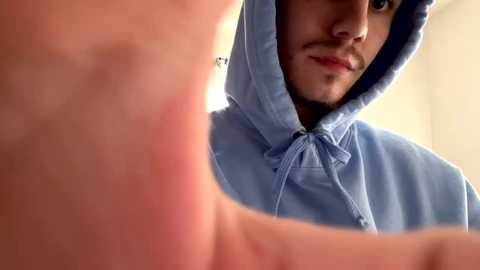 Media: Video of a young man in a blue hoodie, partially cropped, looking introspective, with a blurred background.