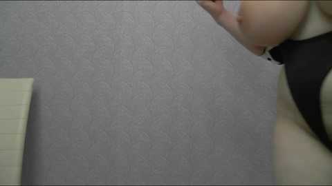 Media: Video of a woman with fair skin, wearing a black sleeveless top, looking down at a light-colored notebook on a textured gray wall.