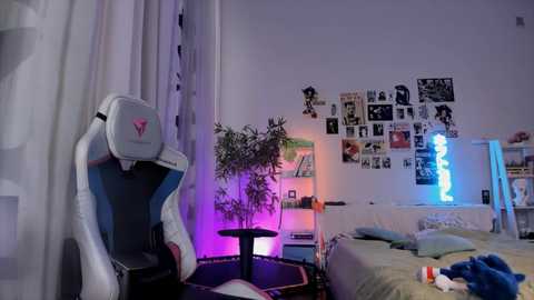 Media: Video of a cozy bedroom with a white gaming chair, purple light, plant, posters, and a bed with blue pillows.