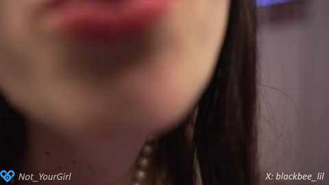 Media: Close-up video of a woman's lips and chin, with a blurred background. She has fair skin, dark hair, and wears red lipstick. Text reads \"Not Your Girl\" and \"X blackbee li.\