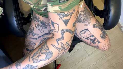 Media: Video of a person with extensive, intricate black ink tattoos on both thighs and legs, wearing camouflage pants and seated on a black office chair.