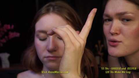 Media: Video of a close-up of two young women, one applying makeup to the other's eye, in a dimly lit room.