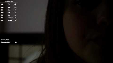 Media: Video of a dimly lit, close-up shot of a person with long, dark hair, partially obscured by shadows. The background is indistinct and dark, with text overlaid, possibly indicating a video game interface.