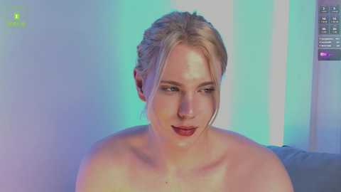 Media: Video of a fair-skinned, blonde woman with auburn hair, topless, in a soft, blue-lit room, with a subtle, playful expression, slightly tilted head, and a hint of makeup.