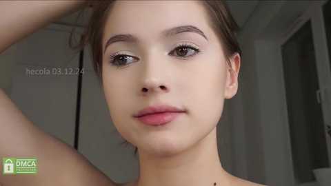 Video of a young woman with fair skin, brown eyes, and short brown hair, wearing natural makeup, in a bathroom with a green DAMEK logo watermark.