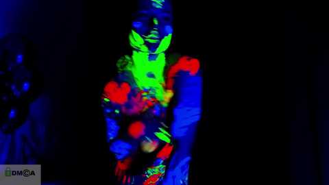 Media: Video of a neon-lit, partially visible person in a bright, vibrant outfit with green, blue, and red lights, standing against a dark background.