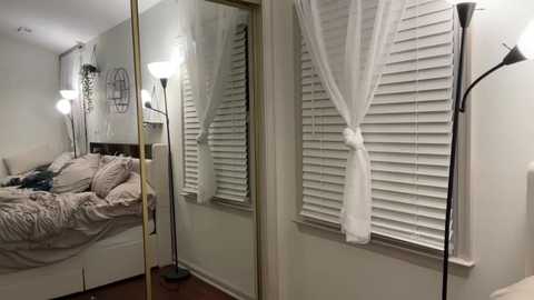 Media: A video of a minimalist, cozy bedroom with beige walls, a bed covered in textured pink bedding, a tall floor lamp, and white sheer curtains.