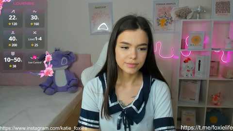 Media: A video of a young woman with long dark hair, wearing a sailor school uniform, in a cozy room with pink neon lights and a plush purple dinosaur.