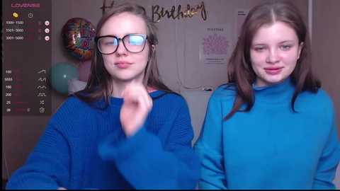 Media: Video of two young women with fair skin and brown hair, one wearing glasses, both in blue sweaters, smiling, in a birthday-themed room with balloons and decorations.