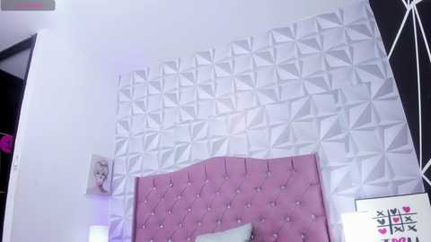 Media: Video of a modern bedroom with a white geometric-patterned wall, pink tufted headboard, pink pillows, and a small framed photo.