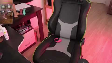 Media: Video of a modern gaming chair with black and gray upholstery, pink controller, and neon accents. Background includes a desk with a monitor, controller, and scattered gaming accessories.