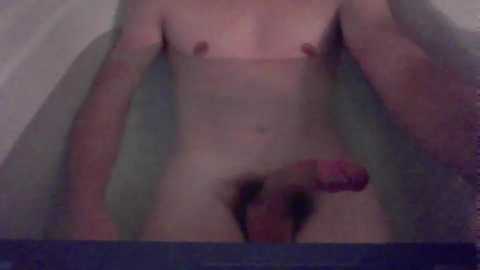 Media: Video of a nude person with light skin, small breasts, and a circumcised penis, submerged in a bathtub. The background is blurred, featuring a white wall.