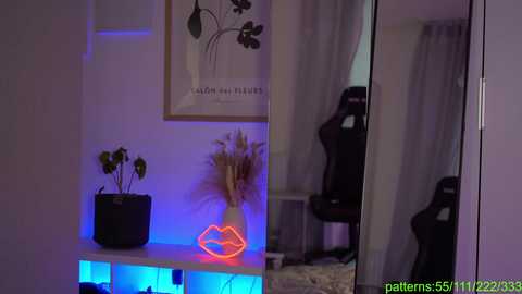 Media: A video shows a cozy room with a minimalist aesthetic. A black plant pot with a potted plant sits on a white shelf, illuminated by blue LED lights. A red neon sign shaped like lips hangs nearby. A framed abstract artwork with a floral design hangs on the wall.