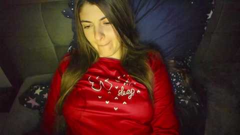 Media: Video of a young woman with long, straight brown hair, lying on a couch, wearing a red sweatshirt with white text and hearts, and a blue pillow.