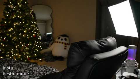 Media: A video of a cozy living room with a decorated Christmas tree, a plush snowman, and a black leather couch. A bright light illuminates the right side, casting a warm, festive ambiance.