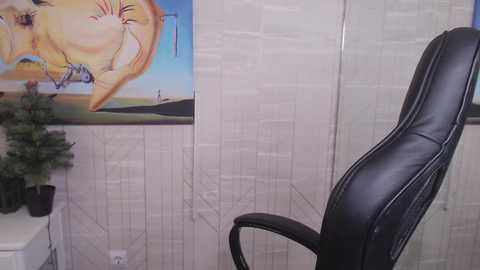 Media: A video of a modern office space with a white textured wall, a black leather office chair, and a colorful beach-themed painting in the background.