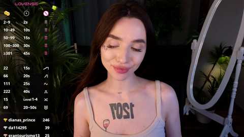 Media: A video of a fair-skinned, long-haired woman with a tattoo reading \"VOS\" on her chest, smiling in front of a mirror, with a camera interface in the background.