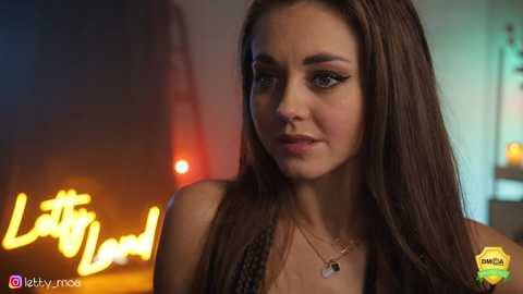 Media: Video of a fair-skinned woman with long brown hair, wearing a sleeveless top, in a dimly-lit bar. Neon \"Little Donut\" sign in the background.