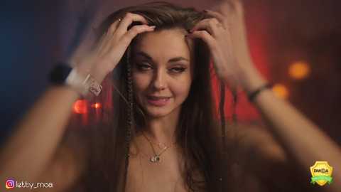 Media: Video of a young woman with long, straight brown hair, wearing a necklace, smiling while two hands brush her hair.