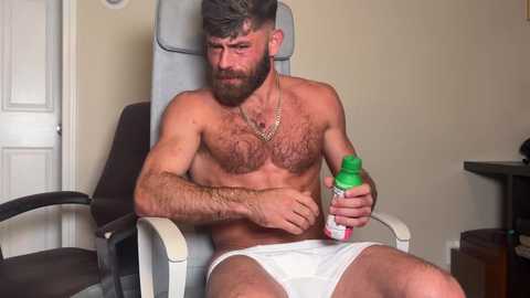 Media: Video of a bearded, hairy-chested man in white briefs, applying cream to his abdomen in a beige room with a gray chair and white door.