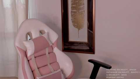 Media: Video of a pink gaming chair with white accents, beige wall with framed leaf artwork, and a black desk chair in a minimalist, softly lit room.