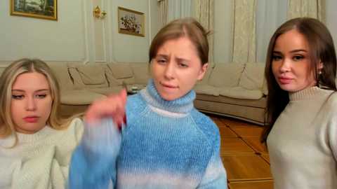 Media: Video of three young women, one wearing a blue and white striped sweater, in a living room with beige furniture and framed pictures on white walls.