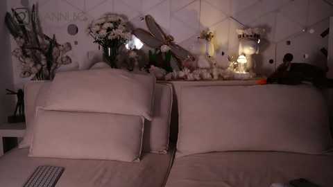 Media: A video of a dimly lit, cozy living room with white furniture, decorative floral arrangements, a small table lamp, and a plush throw blanket.