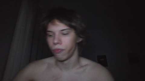 Media: A dimly lit video of a young, shirtless man with curly dark hair, fair skin, and closed eyes, possibly in a bathroom with a towel hanging.