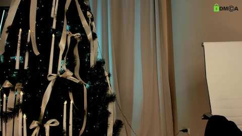 Video of a Christmas tree adorned with white ribbon and candles, set against beige curtains in a dimly lit room. A white projection screen is partially visible on the right.