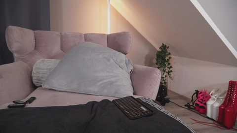 Media: Video of a cozy attic bedroom with a pink velvet sectional sofa, a green plant, and a laptop on a black keyboard, featuring a warm, ambient light and modern decor.