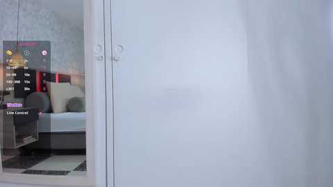 Media: Video of a modern, minimalist bedroom with a white bed, beige pillows, and a small TV on the nightstand. The room has a subtle floral wallpaper, and a door leads to a bathroom with a frosted glass door.