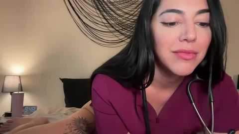 Media: Video of a Latina woman with long black hair, wearing a burgundy top, listening to a stethoscope, in a beige bedroom with a black lamp and abstract wall art.