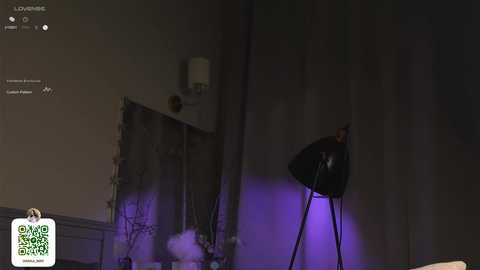 Media: A video of a dimly lit room with a large black light fixture emitting a purple glow. In the background, a white wall and a mirror reflect the light, creating a moody ambiance.