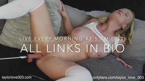 Video of a blonde woman with medium breasts, lying on a grey couch, wearing white panties and thigh-high socks. Text overlay: \"Live Every Morning at 5 AM (EST) All Links in Bio.\