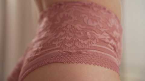 Media: A close-up video of a light-skinned woman's torso wearing a pink lace bra with floral patterns, partially visible under her skin. The background is blurred, focusing on the intricate lace design.