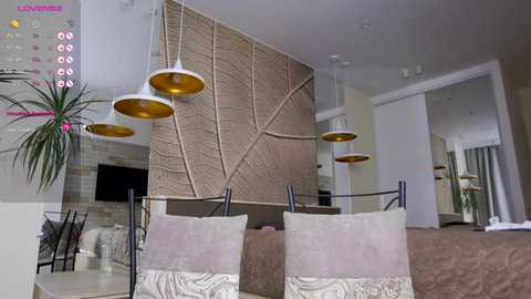 Media: Modern, minimalist dining room with beige walls, a large woven art panel, potted plants, two white chairs with beige cushions, and three hanging pendant lights with gold interiors.