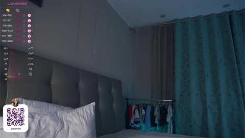 Media: A dimly-lit, modern bedroom with a dark headboard, white pillow, and teal curtains. A QR code is displayed on the left, with a notification indicating \"Live Chat\" on the top left.