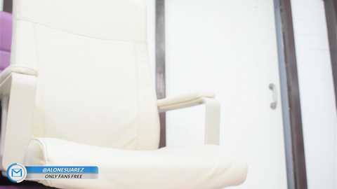 Media: Video of a modern, white leather office chair with armrests, placed in a bright, minimalist room with a white wall and dark wooden frame.