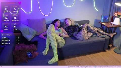 Media: Video of two women in neon green, fishnet bodysuits, lounging on a blue sofa in a dimly lit, purple-lit room.