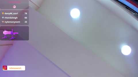 Media: Video of a modern, well-lit room with two bright white ceiling lights. A small, pink toy airplane sits on the floor in the left corner. The background includes a blurred, red-framed TV screen.