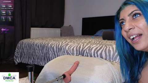 Media: A video shows a woman with vibrant blue hair and fair skin, smiling, while holding a realistic, erect penis-shaped vibrator. The background features a zebra-patterned bed and dark curtains.