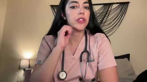 Media: Video of a young Latina woman with long black hair, wearing a pink scrub top, examining her mouth with a stethoscope in a bedroom with a bed, lamp, and hanging net.