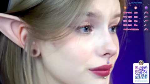 Media: Video of a young, fair-skinned woman with pointed elf ears, light brown hair, and a nose ring, wearing makeup. Background is a purple gradient with text overlays and a QR code.