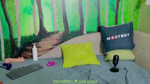 Media: A vibrant video of a cozy bedroom with a green forest mural, a beige couch, a bright green pillow, a grey keyboard, and a black microphone.