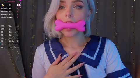 Media: Video of a blonde woman with a pink bone gag, wearing a sailor outfit, with a chat window overlay.