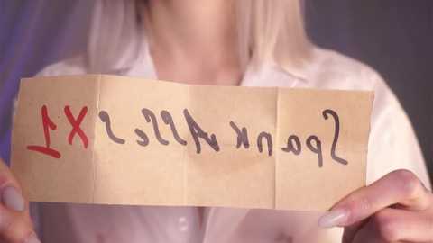 Media: Video of a person holding a piece of brown paper with \"X\" and \"XX\" in red ink, wearing a white blouse, blurry background.