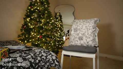 Media: Video of a cozy bedroom with a lit Christmas tree, a white chair adorned with a patterned pillow, and a bed covered in floral bedding.