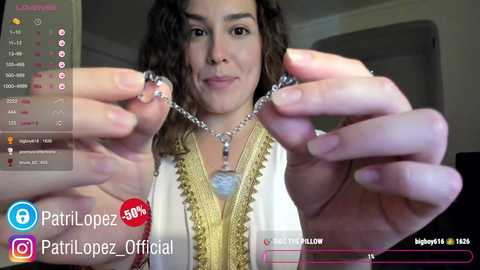 Media: A video of a woman with curly hair, holding a silver necklace with a blue pendant, indoors, with social media icons and a live chat window overlay.