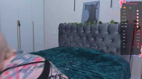 Media: Video of a modern bedroom with a gray tufted headboard, teal blanket, and a woman in a floral dress. A digital screen displays a virtual reality interface.