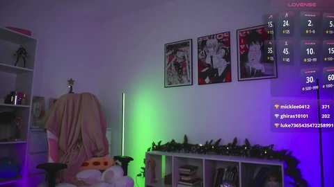 Media: Video of a dimly-lit room with a plush chair, a white shelf, and a Christmas tree. The walls are adorned with framed anime posters and a green neon light.